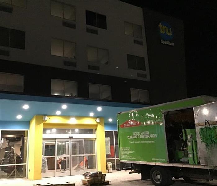 A green box truck parked in front of a hotel at night