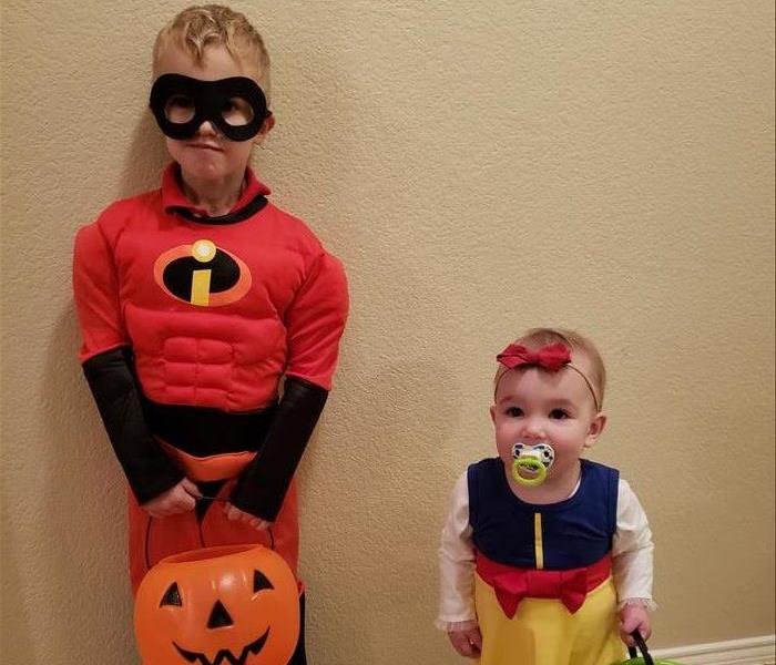 A boy dressed as Mr. Incredible and a toddler aged girl dressed as snow white holding Halloween candy pails.
